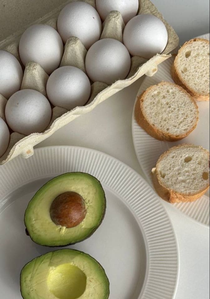 Huevos, aguacate y pan sobre una mesa clara, con luz natural.