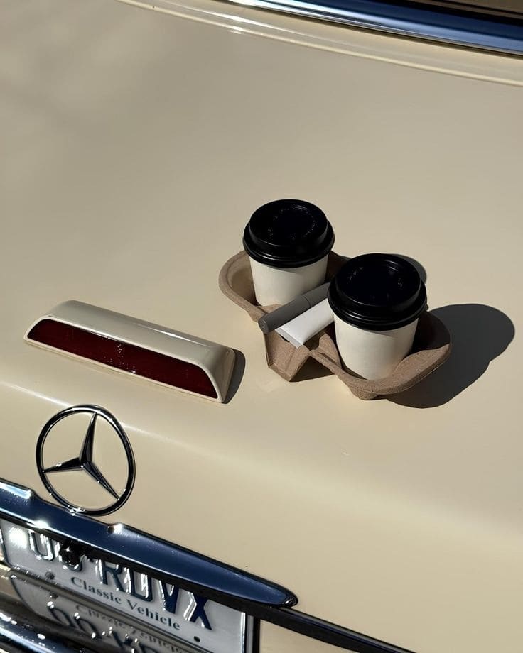 Dos cafés para llevar sobre la cajuela de un auto clásico color crema.